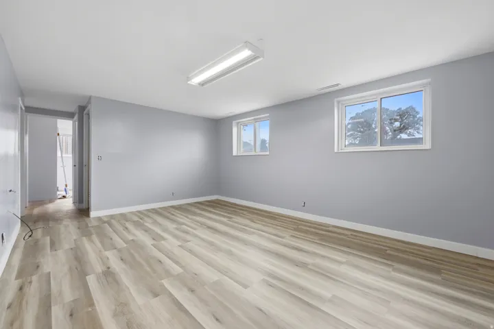 Spacious room with wood-finish flooring, light gray walls, white trim, and two windows