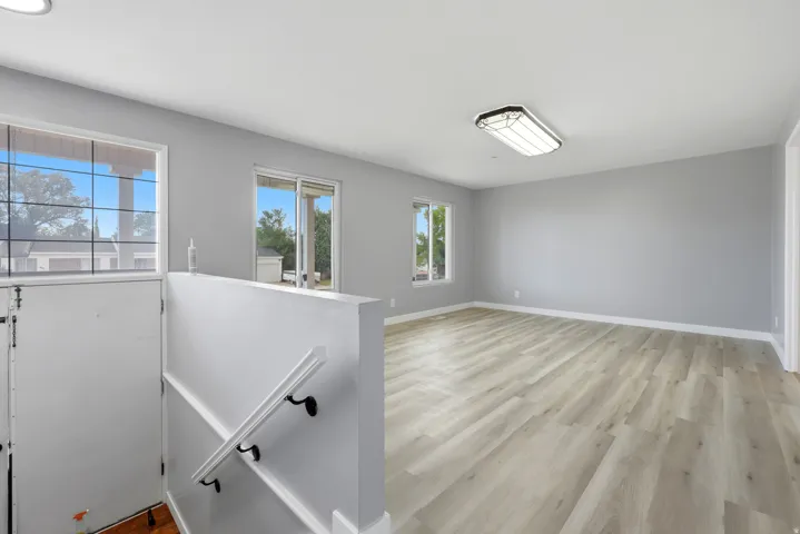 Spacious room featuring light wood-finish flooring, neutral gray wall paint, multiple windows, and a sliding glass door