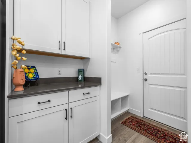 Entryway featuring a paneled door, wood-finish flooring, built-in storage bench, and white cabinetry with dark hardware and a dark countertop