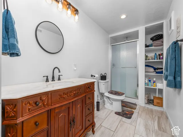 Bathroom featuring a wood-finish vanity with an integrated sink and light-colored countertop, framed mirror, and a shower with a sliding glass door