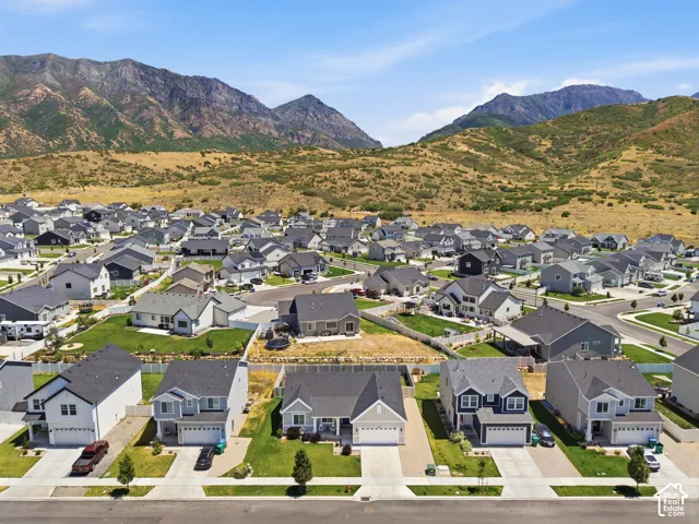 Residential community with a variety of architectural styles, manicured lawns, and paved driveways, set against a backdrop of natural mountain terrain
