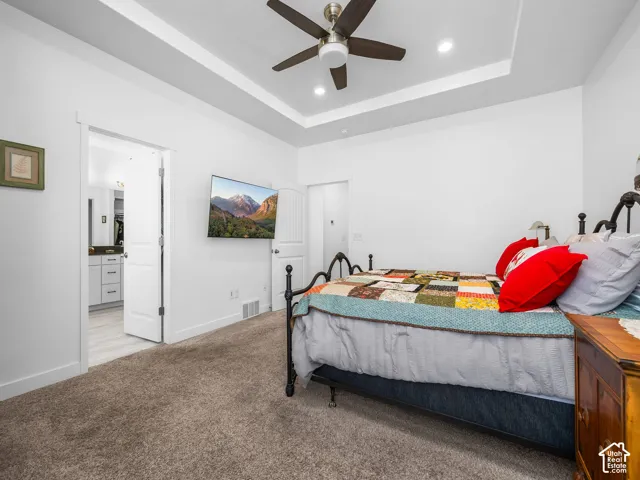 Bedroom featuring neutral-toned carpeting and a tray ceiling with a ceiling fan