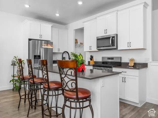 Modern kitchen featuring white shaker cabinetry, stainless steel appliances, dark countertops, and wood-finish flooring