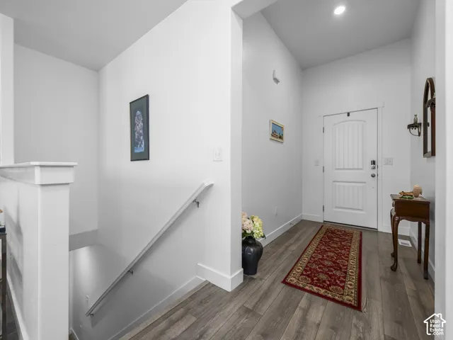 Bright entryway featuring wood-finish flooring, a white paneled front door, and a staircase with a white railing