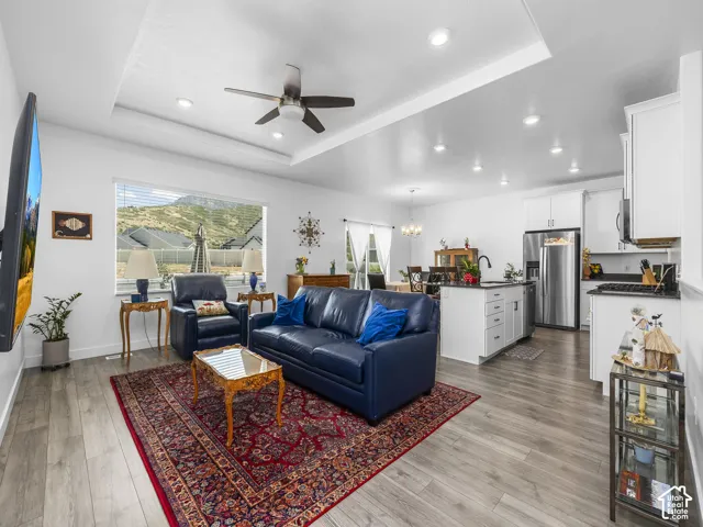 Open-concept living space featuring wood-finish flooring, recessed lighting, and a tray ceiling with a ceiling fan