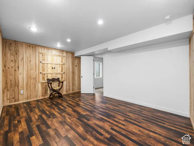 Spacious room featuring wood-finish flooring, a paneled accent wall with a built-in cabinet, and recessed ceiling lighting