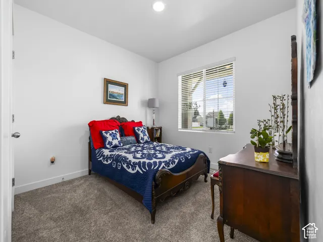 Carpeted bedroom with a single window, white walls, and bright overhead lighting