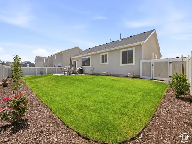 Spacious backyard featuring a large green lawn, a concrete patio, and mature landscaping with a wood chip border