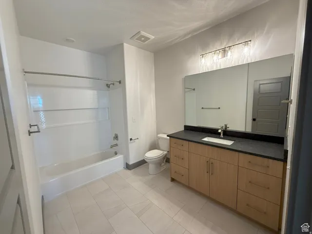 Bathroom featuring a light wood-finish vanity with ample storage, a dark countertop, and a rectangular undermount sink