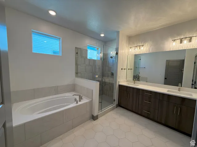 Spacious bathroom featuring a built-in soaking tub, glass-enclosed shower with tiled walls, dual vanity with undermount sinks and quartz countertops, and hexagonal floor tiling