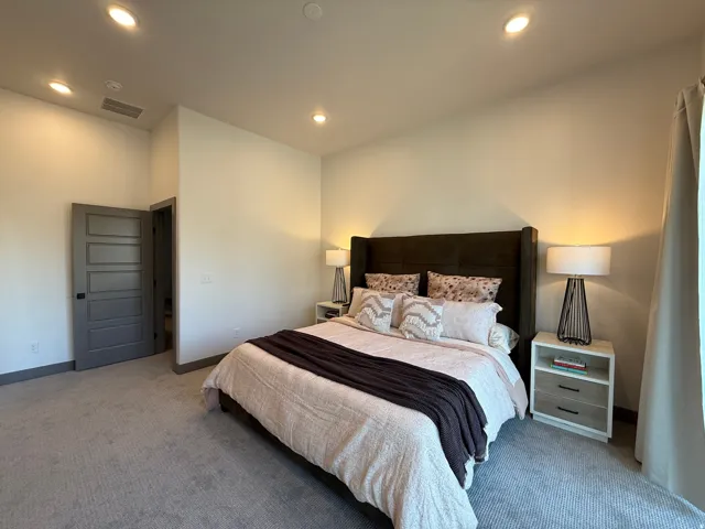 Carpeted bedroom with recessed lighting and a tall, upholstered headboard