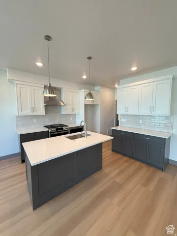 Modern kitchen featuring a central island with an integrated sink, light-toned wood-finish flooring, two-tone cabinetry, quartz countertops, and a tiled backsplash