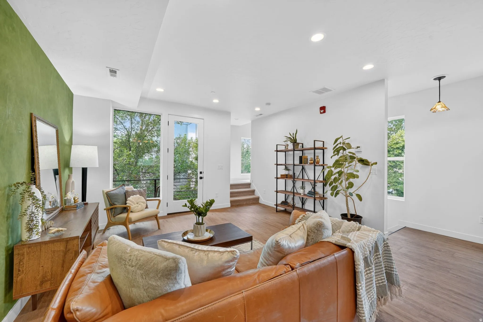 Open concept living space featuring wood-finish flooring, a full-lite glass door opening to an exterior balcony, recessed lighting, and a prominent accent wall