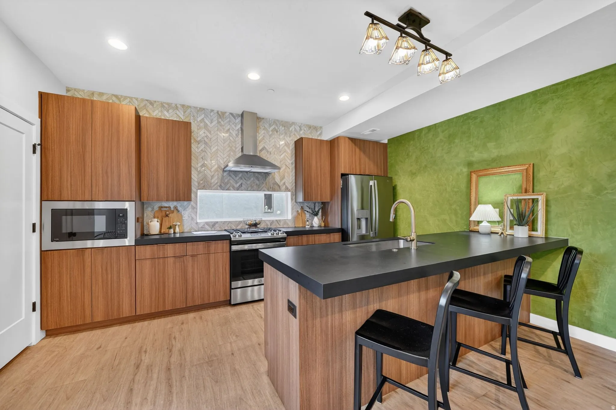 Modern kitchen featuring wood-finish cabinetry, dark countertops, and stainless steel appliances including a built-in microwave and range hood