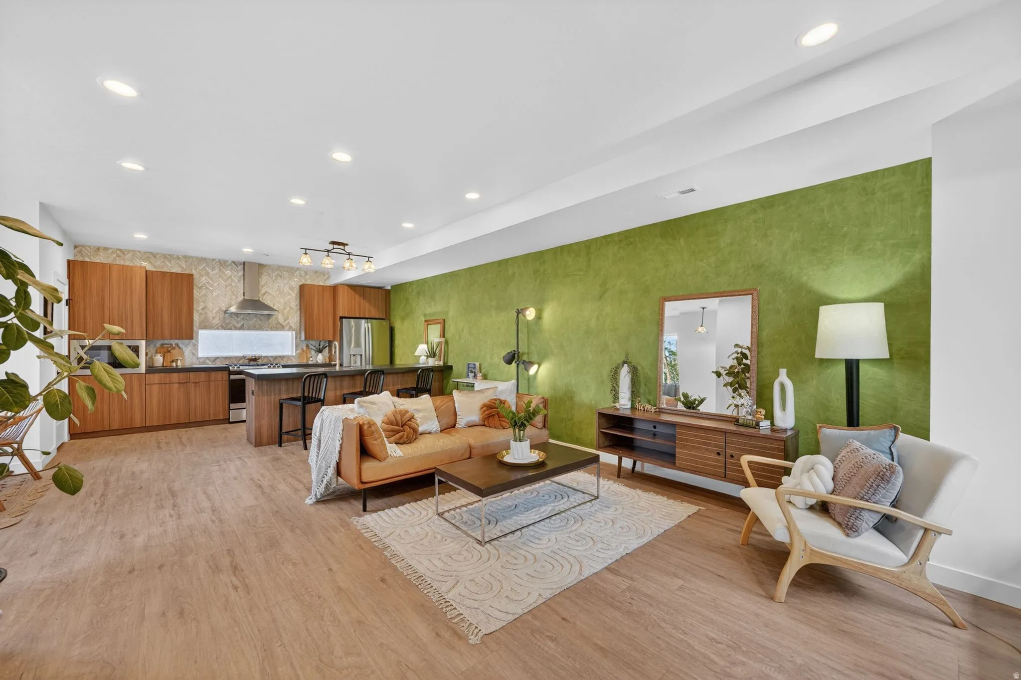Open-concept living space featuring wood-finish flooring, recessed lighting, and a textured green accent wall
