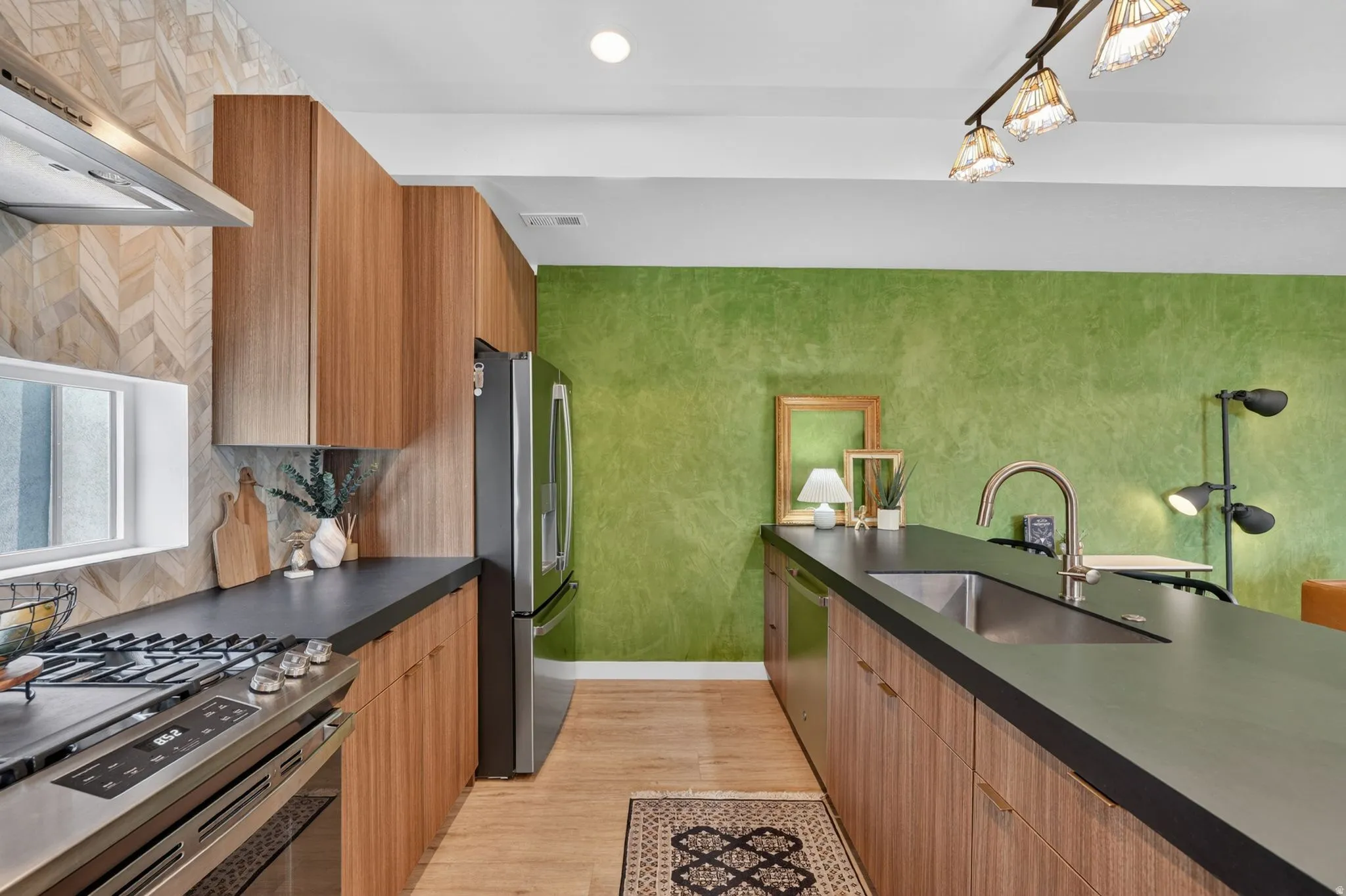Modern kitchen featuring wood-finish cabinetry, dark countertops, a stainless steel gas range, and a coordinating stainless steel refrigerator