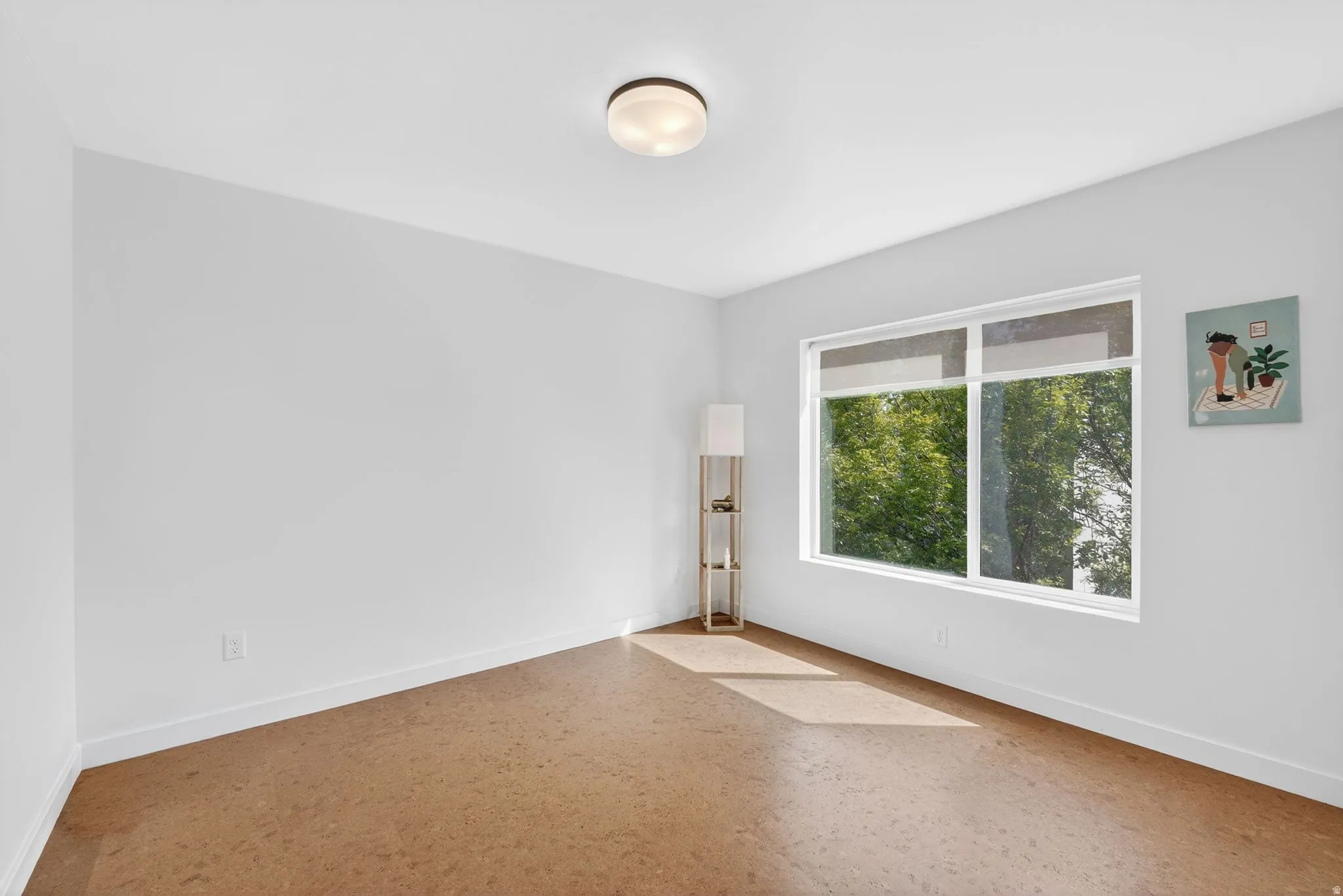 Bright room featuring a large window, cork flooring, white walls, and a flush mount ceiling light fixture