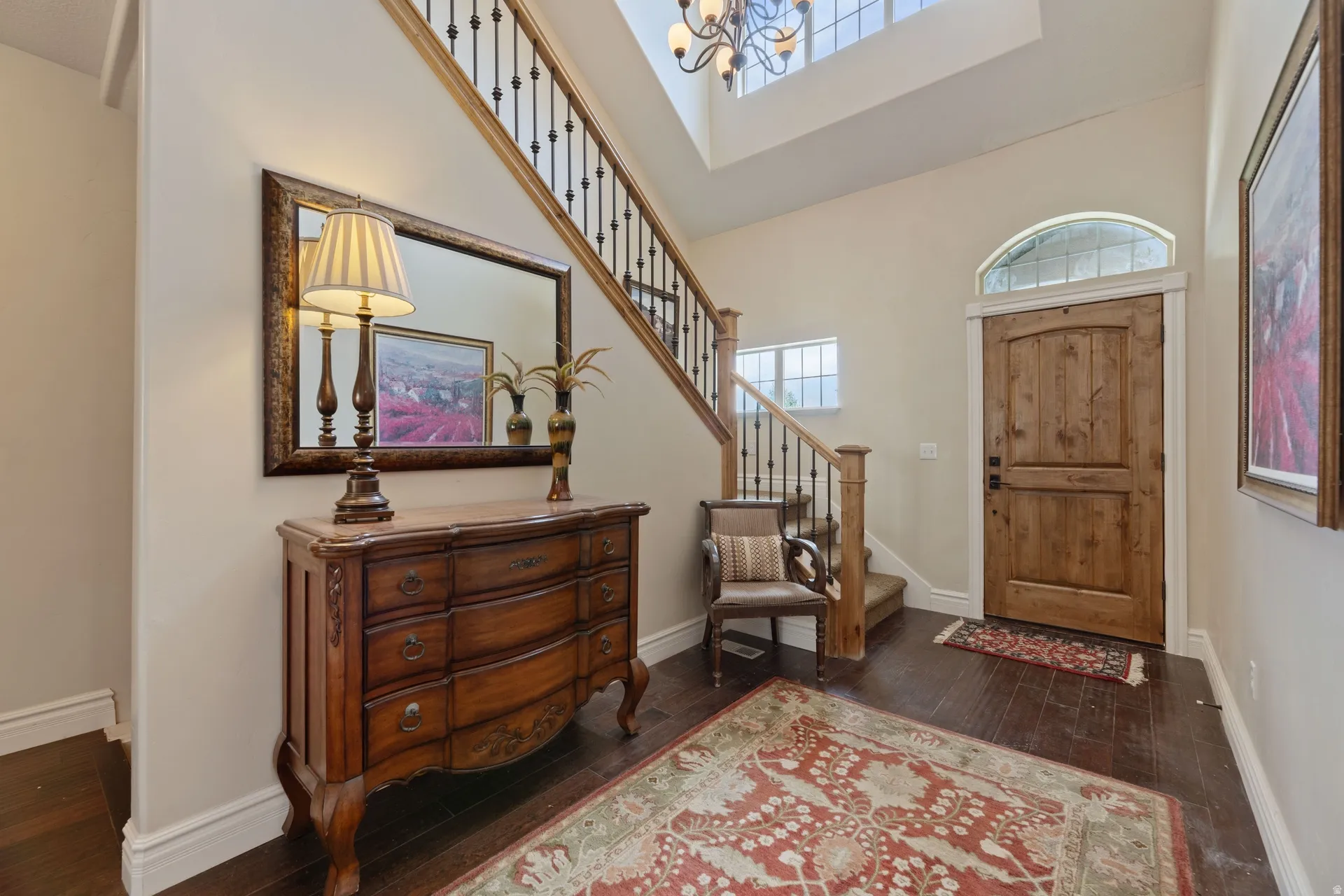 Grand entryway featuring a solid wood door with an arched transom window, dark wood-finish flooring, and a staircase with wrought iron balusters