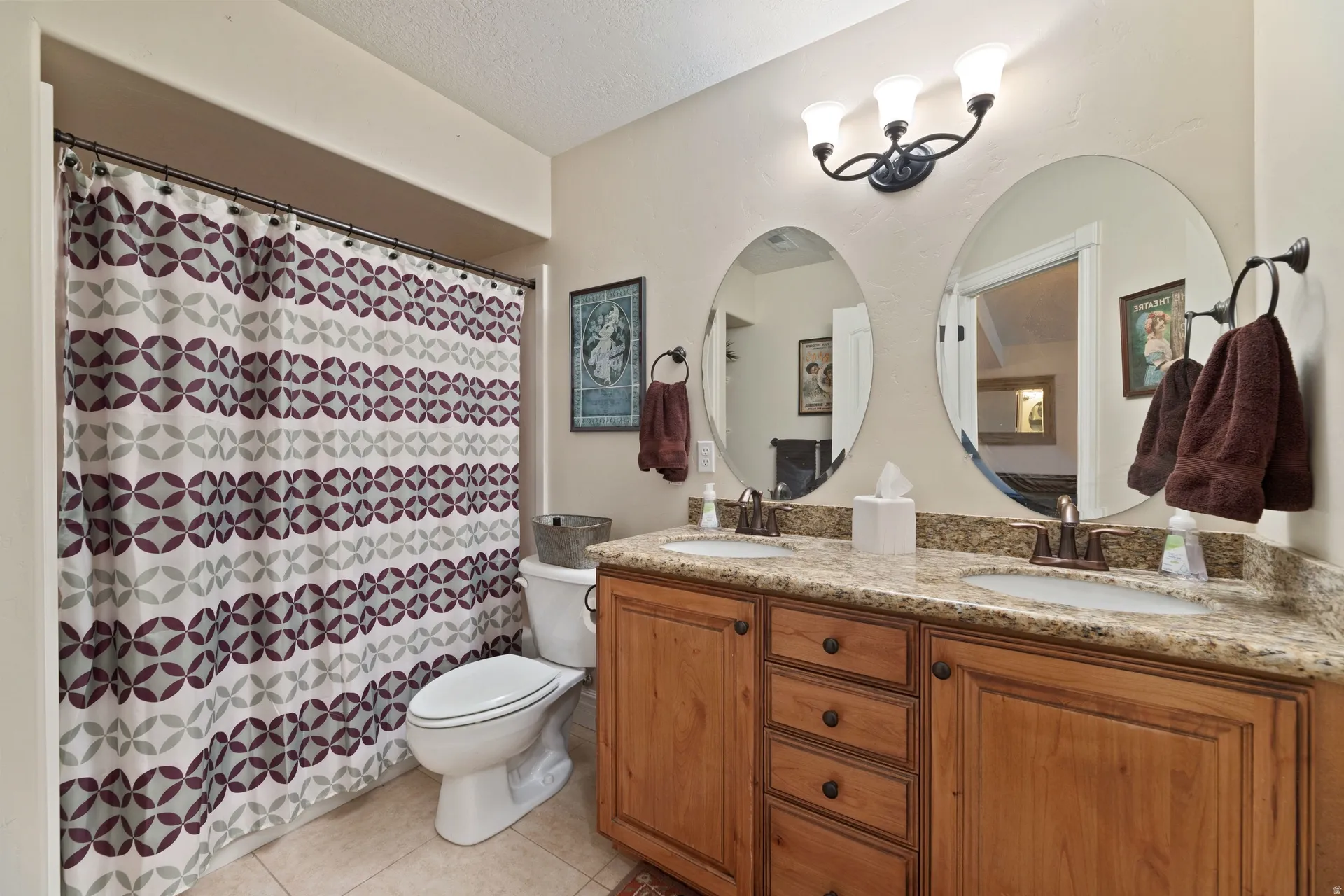 Bathroom featuring a dual vanity with a patterned countertop, two oval mirrors, and a three-light fixture