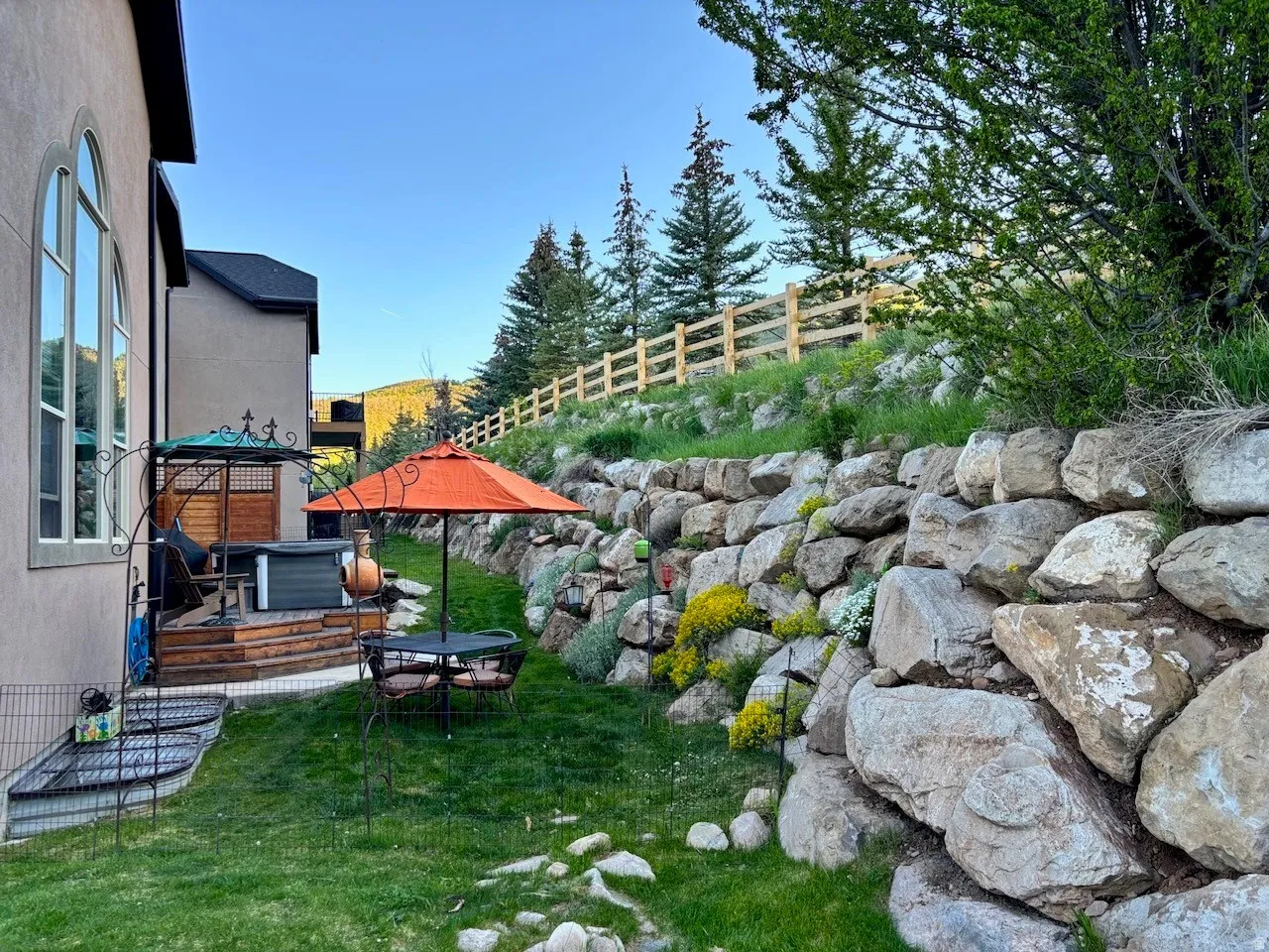 Tiered backyard featuring a rock retaining wall with established plantings, a wooden deck