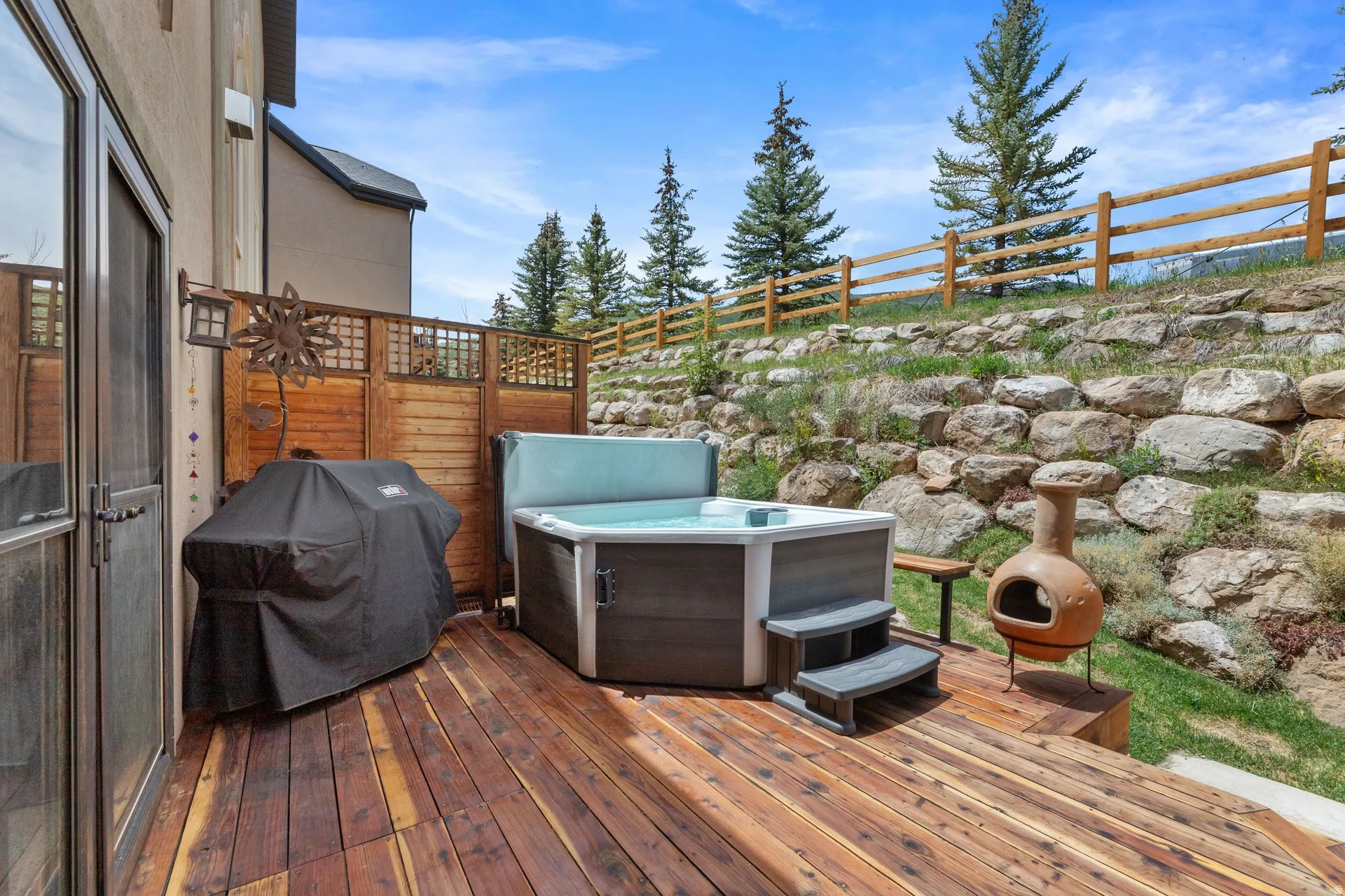 Just off Primary Suite, spacious outdoor deck featuring a hot tub, wood privacy screen, and exterior door