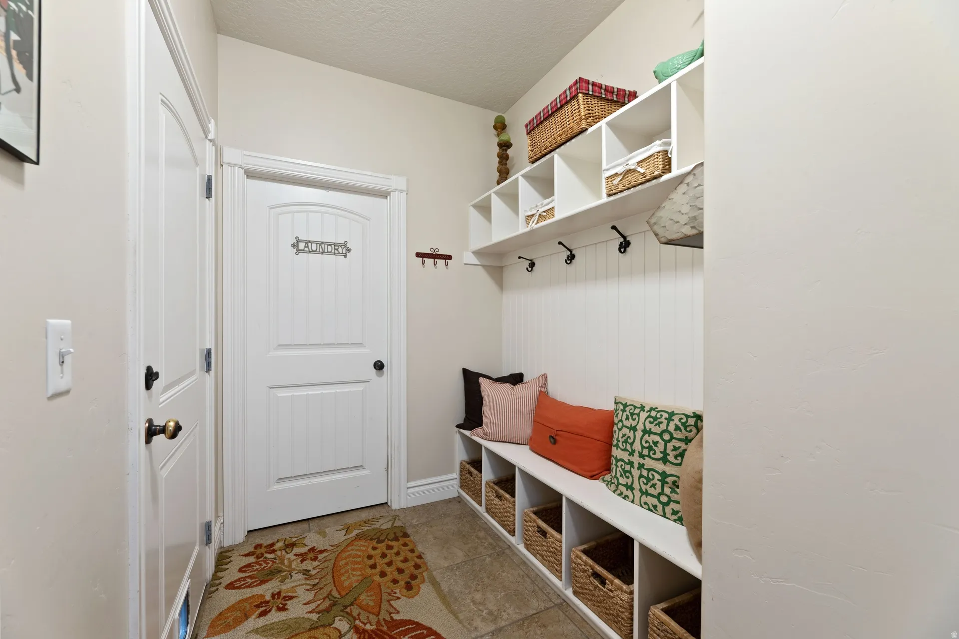 Hallway entry featuring tile flooring, white built-in storage bench, white beadboard wall paneling, and white overhead shelving