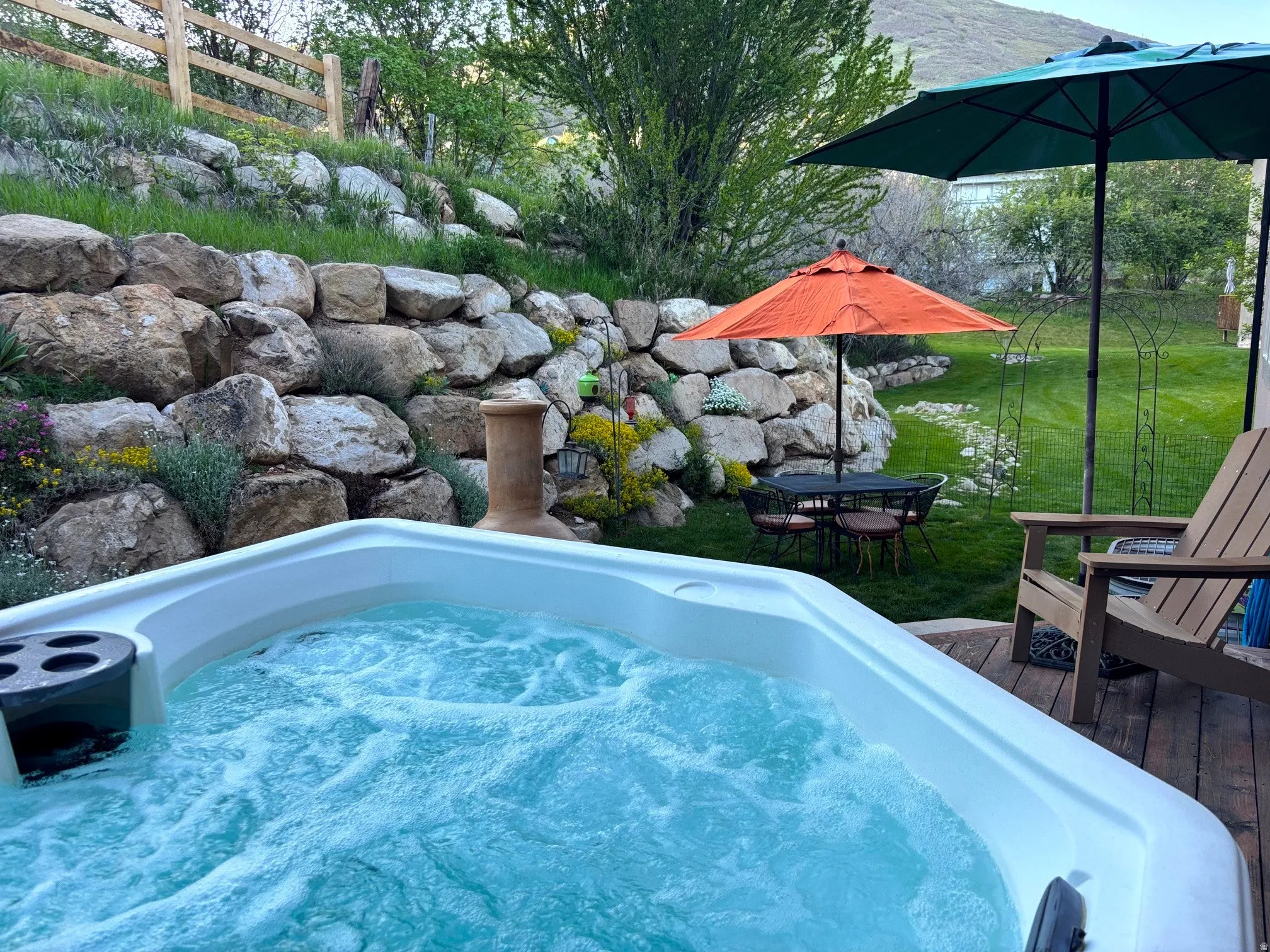 Backyard oasis featuring a bubbling hot tub, a multi-tiered rock retaining wall, a slatted wood privacy fence, and a spacious wood-finish deck