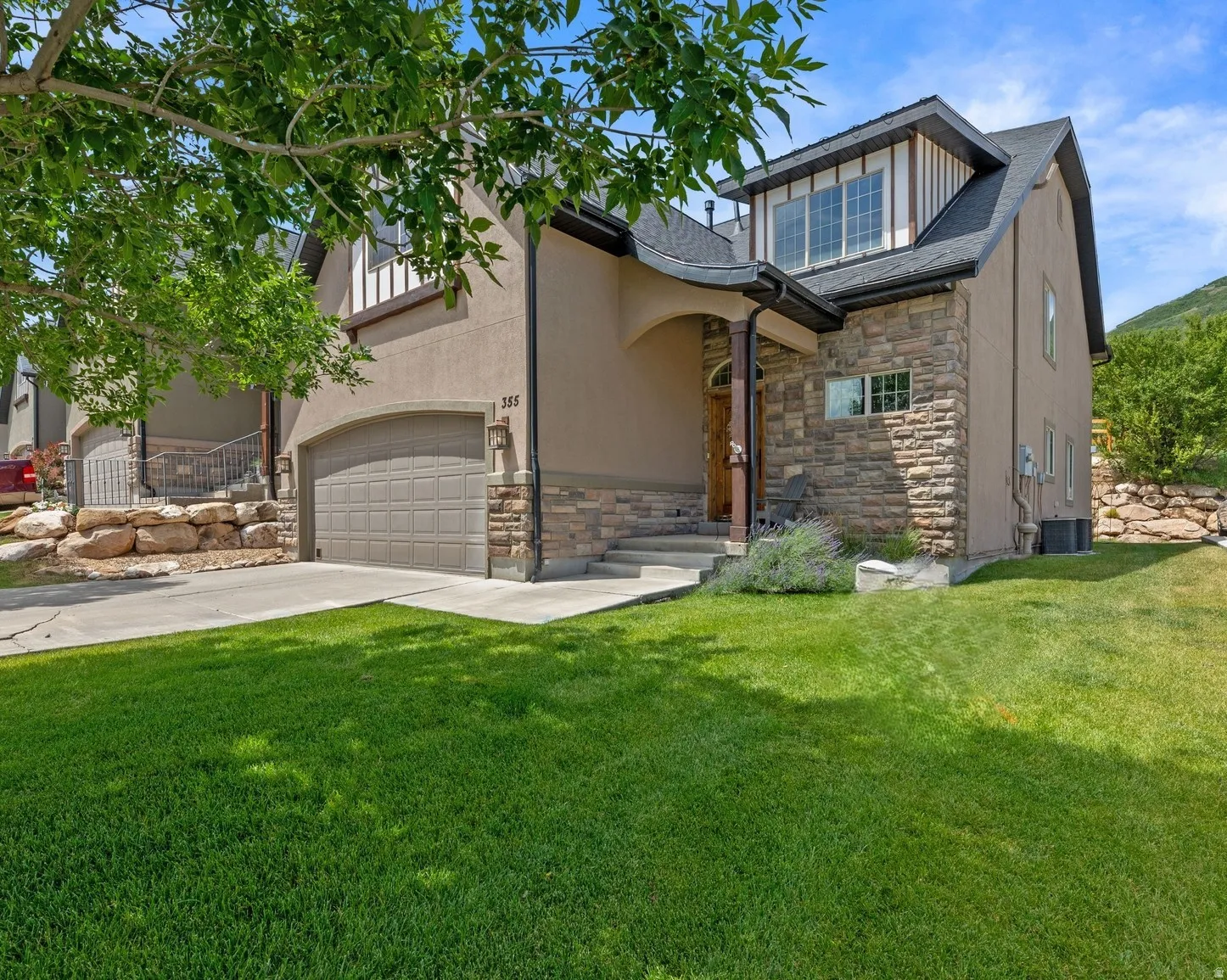 End Unit. Stucco and stone facade home featuring an arched entryway, an attached 2-car garage, a dormer window, concrete steps, and a grassy front yard