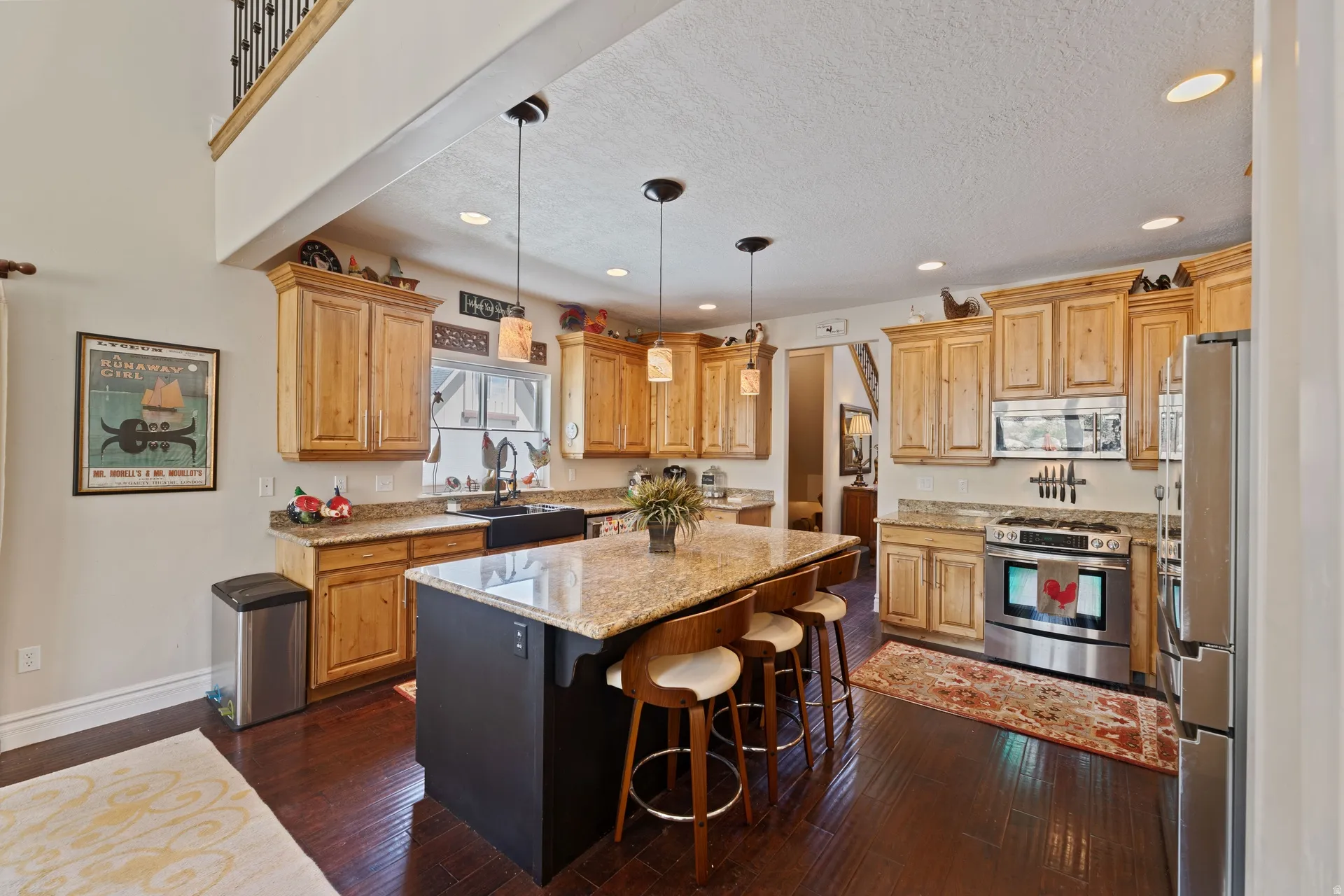 Spacious kitchen featuring rich wood-finish flooring, light wood cabinetry, granite countertops, and stainless steel appliances