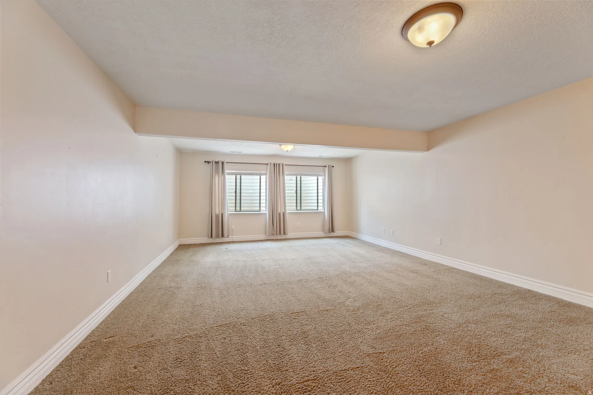 Spacious room featuring neutral carpeting, light-toned walls, and white baseboards
