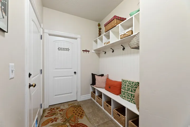 Hallway entry featuring tile flooring, white built-in storage bench, white beadboard wall paneling, and white overhead shelving