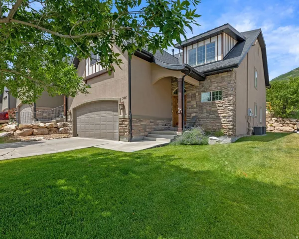 End Unit. Stucco and stone facade home featuring an arched entryway, an attached 2-car garage, a dormer window, concrete steps, and a grassy front yard