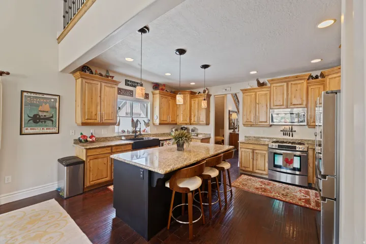 Spacious kitchen featuring rich wood-finish flooring, light wood cabinetry, granite countertops, and stainless steel appliances
