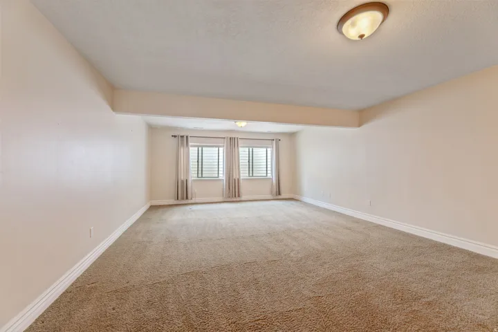 Spacious room featuring neutral carpeting, light-toned walls, and white baseboards