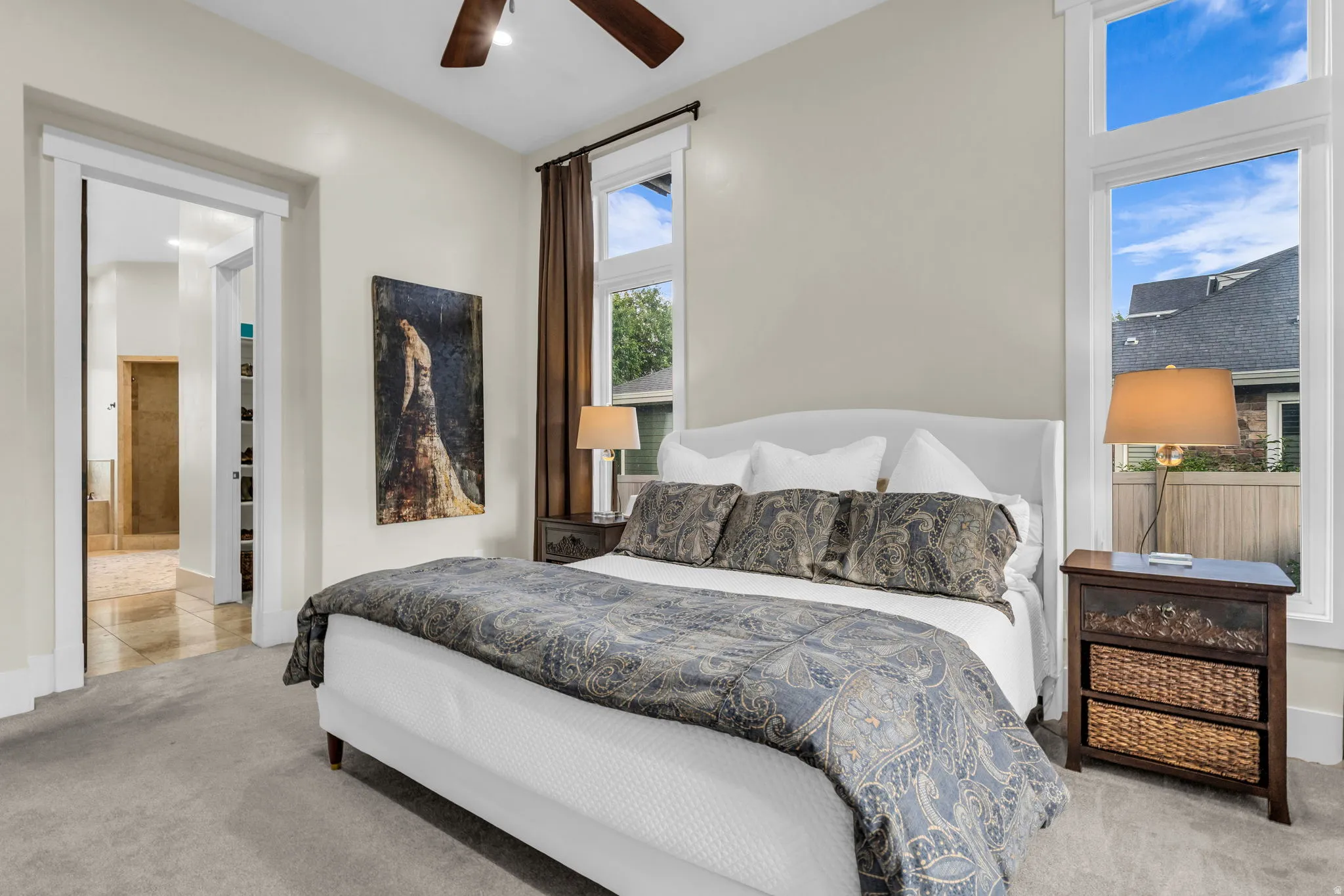 Carpeted room featuring a ceiling fan, dual large windows, and a wide doorway opening to a tiled area