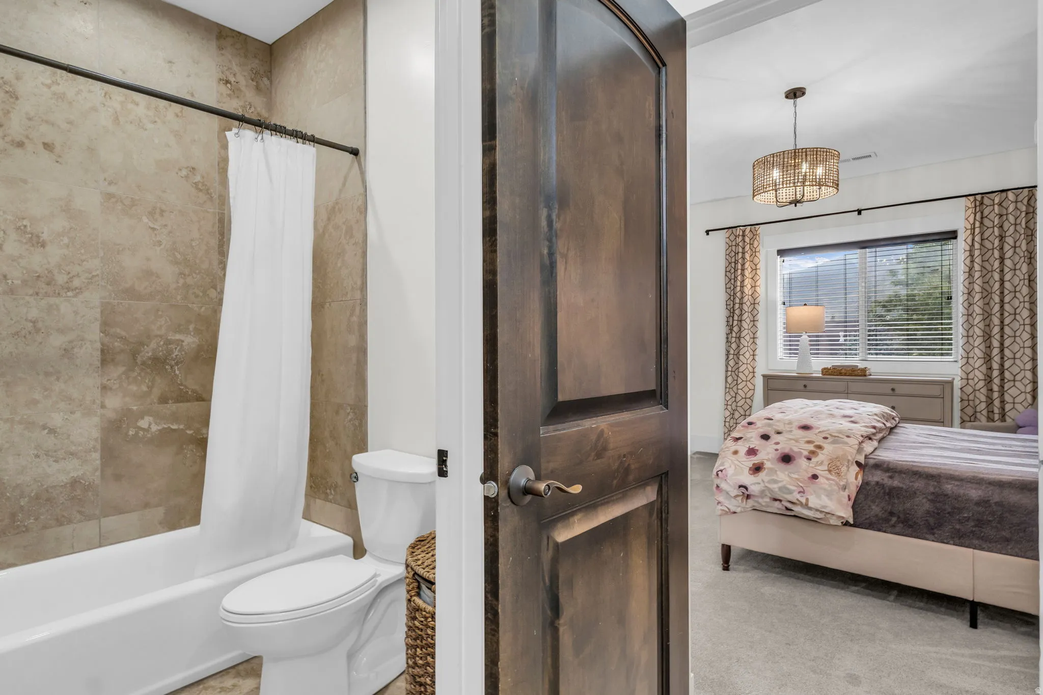 Bathroom featuring a full-size tub with a shower, floor-to-ceiling tile surround, and a white toilet