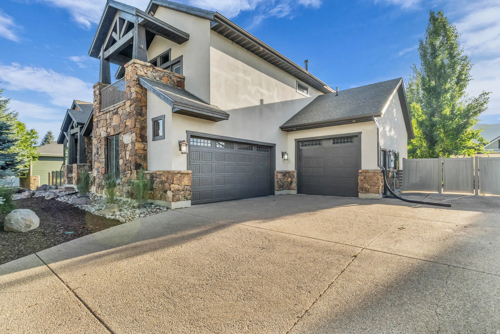 Stucco and natural stone exterior featuring a multi-car driveway, dark garage doors, and a decorative balcony with exposed beams