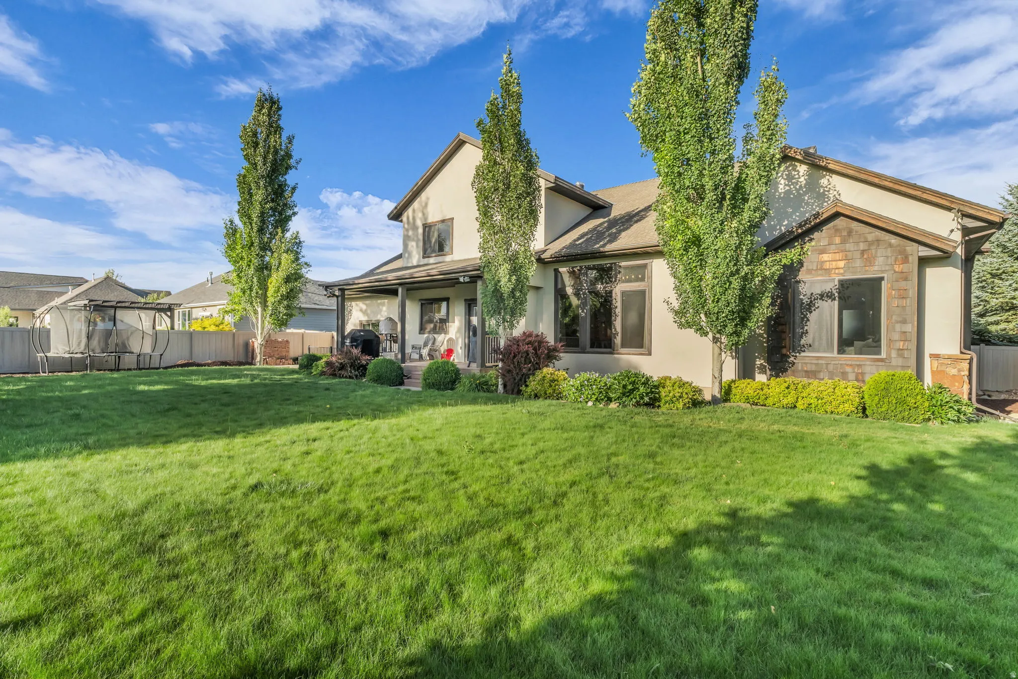 Expansive rear yard with a manicured lawn, established landscaping, and mature trees