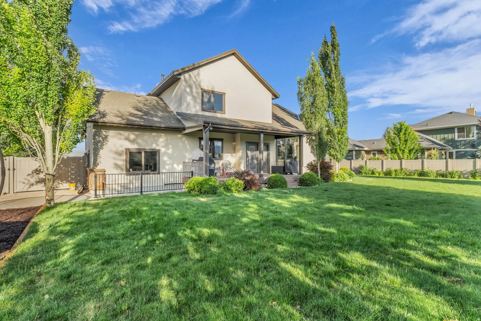 Expansive backyard featuring a manicured lawn, established trees, and a covered patio area with direct property access