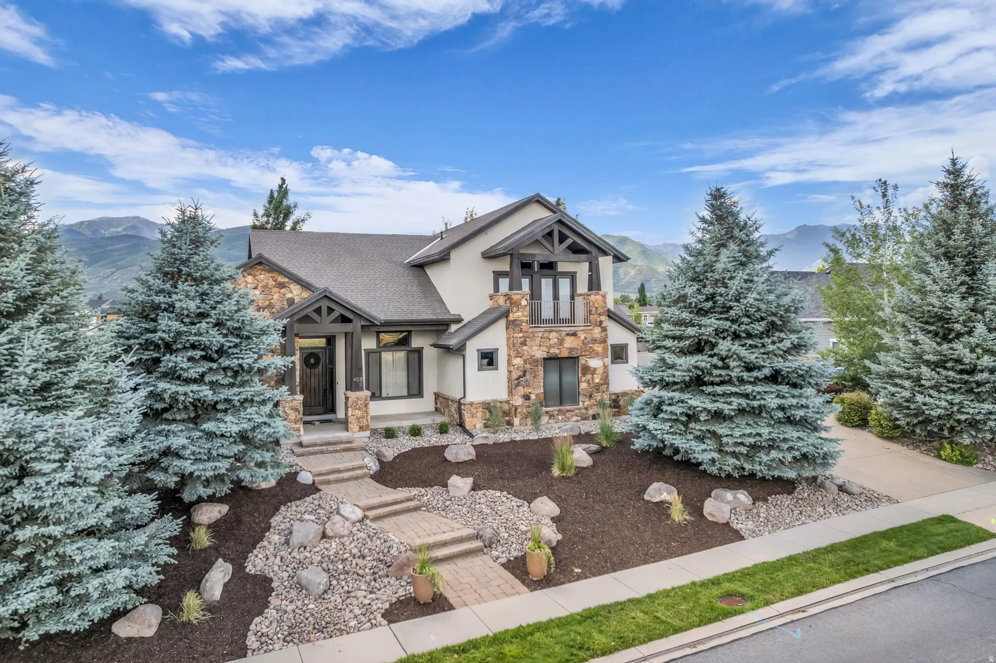 Multi-level residence featuring a blend of stucco and stone cladding, dark trim accents, and a prominent front entrance with a covered porch