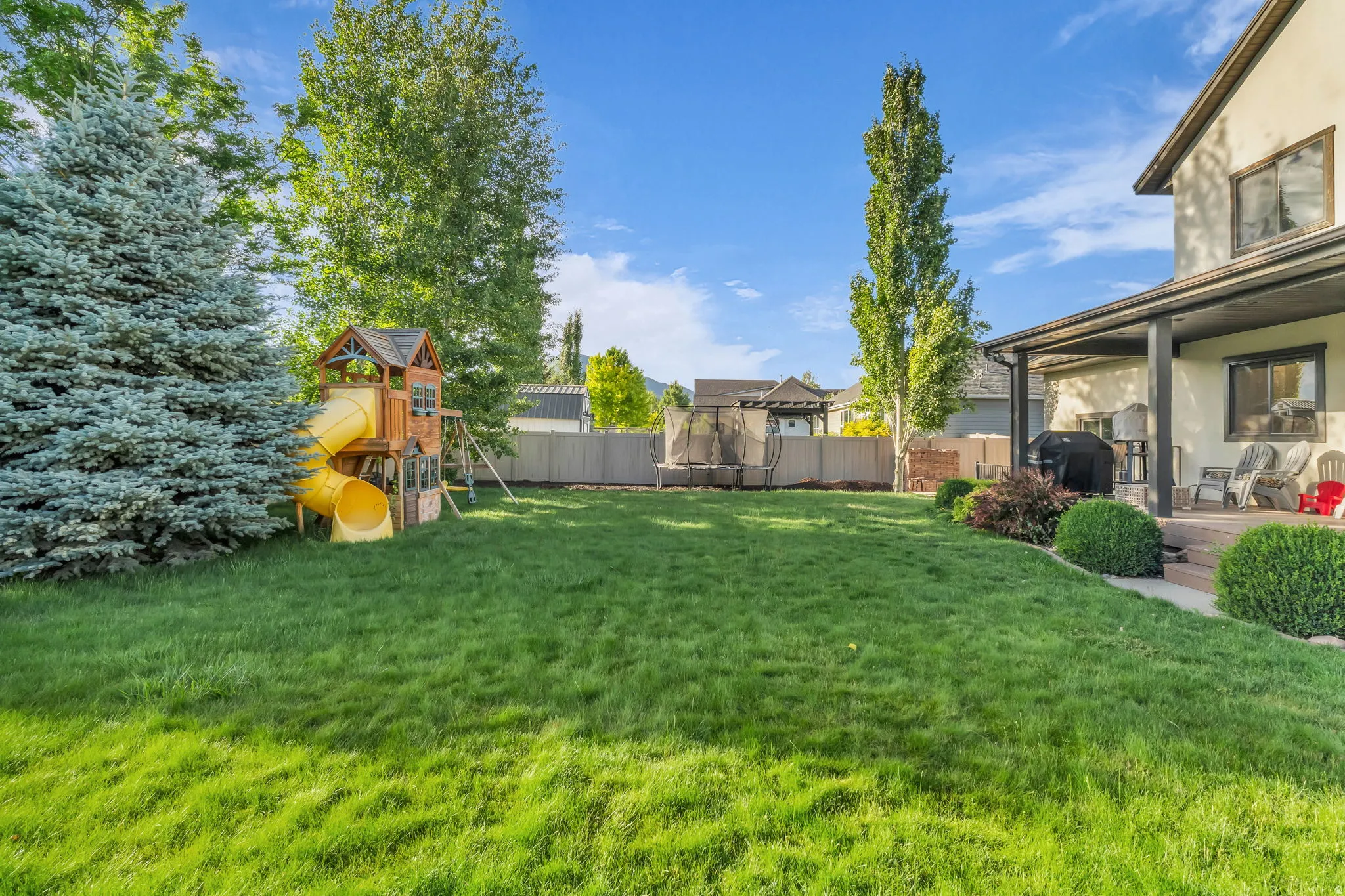 Expansive green lawn with mature trees and a covered patio area