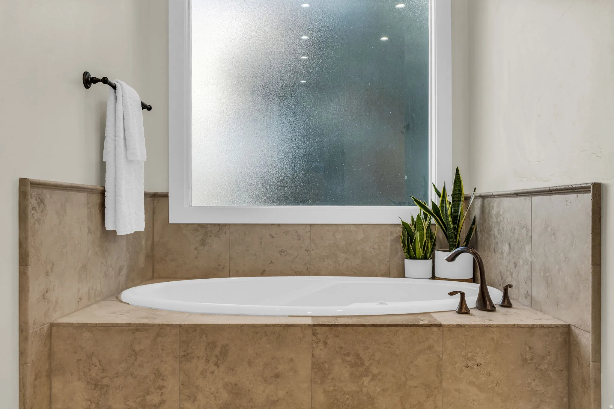 Built-in soaking tub with a tiled surround, frosted window, and bronze-finish fixtures