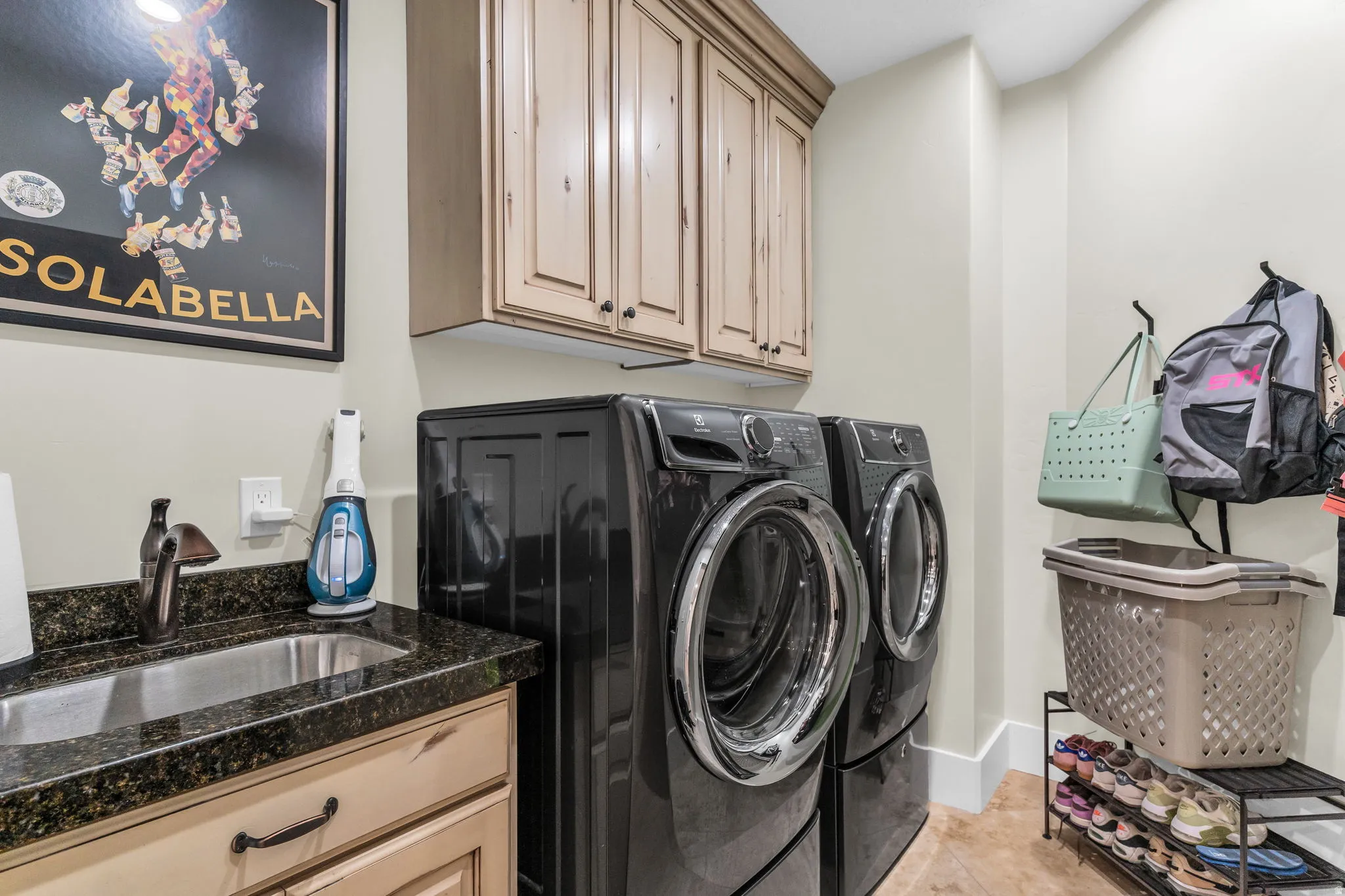 Utility room featuring a utility sink, dark granite-style countertop, and light wood-finish cabinetry