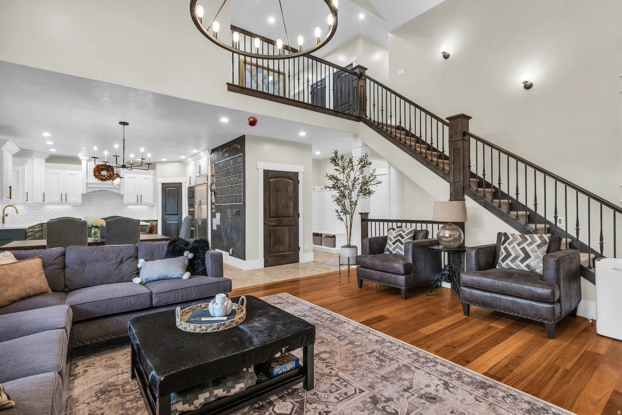 Open-concept living space featuring wood-finish flooring, a grand staircase with dark wood newel posts and metal balusters, and a contemporary chandelier