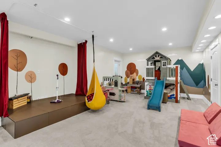 Spacious recreation room featuring light gray carpeting, recessed ceiling lighting, and a raised stage area with red curtain accents