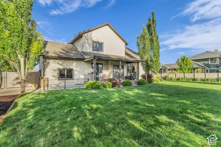 Expansive backyard featuring a manicured lawn, established trees, and a covered patio area with direct property access