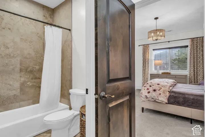 Bathroom featuring a full-size tub with a shower, floor-to-ceiling tile surround, and a white toilet