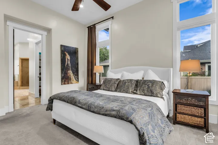 Carpeted room featuring a ceiling fan, dual large windows, and a wide doorway opening to a tiled area