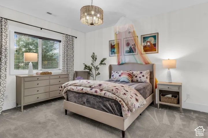 Spacious bedroom featuring plush gray carpeting, a large window with blinds, and white walls