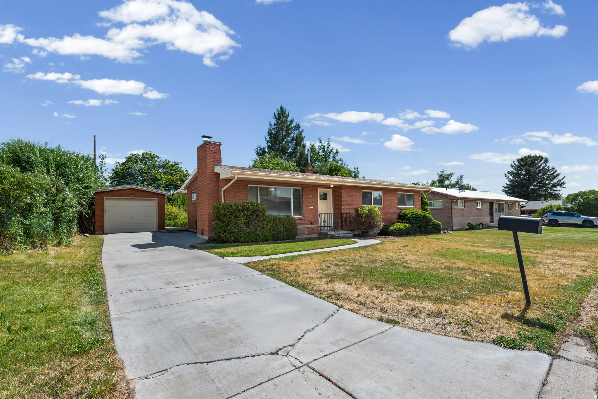Brick ranch-style home featuring a paved driveway, detached garage, and mature shrubbery